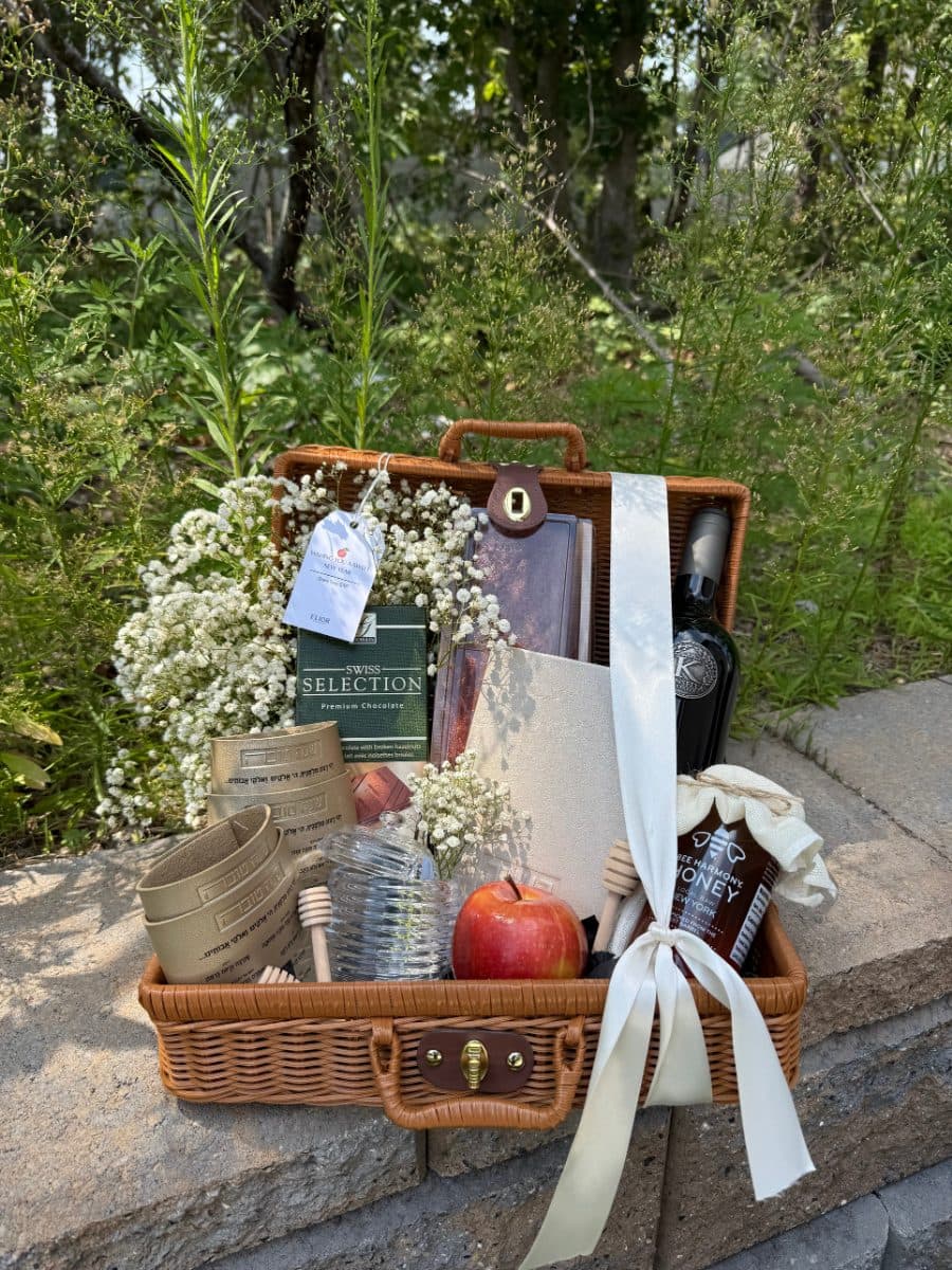 The Luxe — a keepsake wicker suitcase with gold leather simanim napkin wraps, premium wine, honey dish, Swiss chocolates and a leather booklet